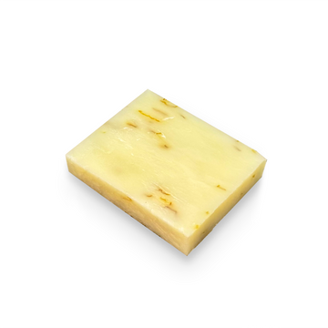 A rectangular bar of pale yellow soap with small golden-yellow botanical inclusions, shown on a plain white background.