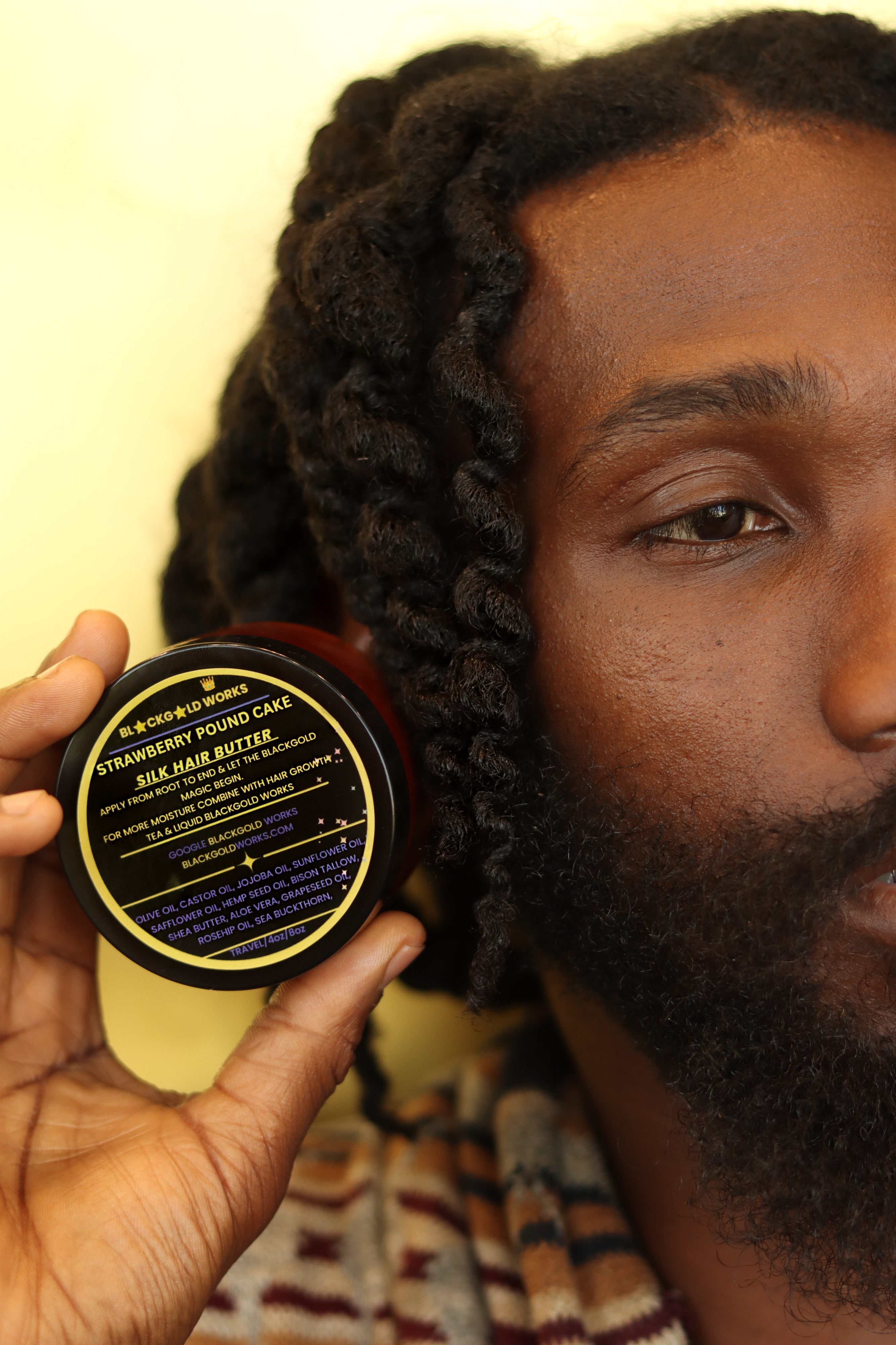 Person holding Black gold work's silk hair butter product jar in hand, with label facing forward.