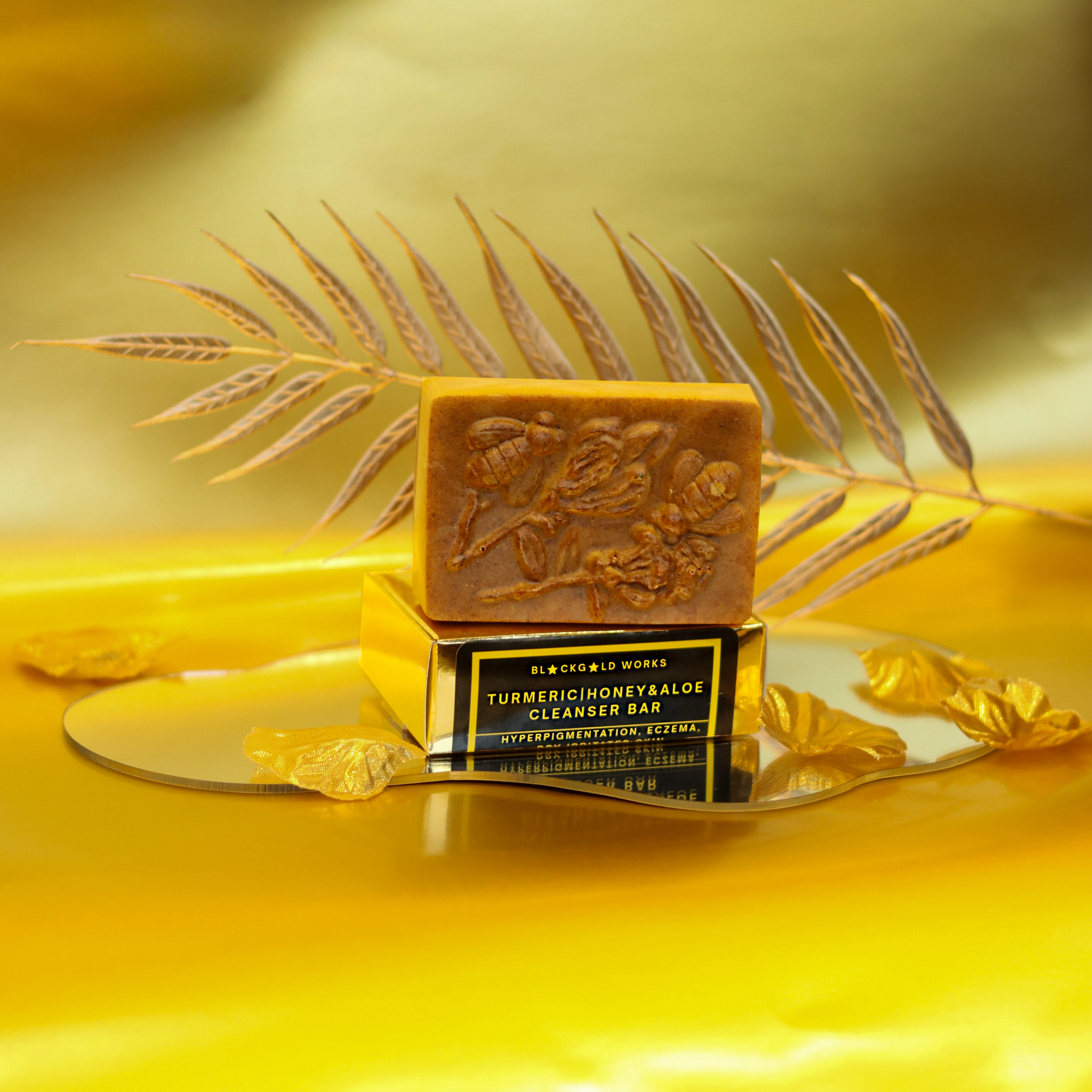 Organic turmeric honey aloe cleanser bar with embossed floral design on top of a gold box with a black and yellow label.
