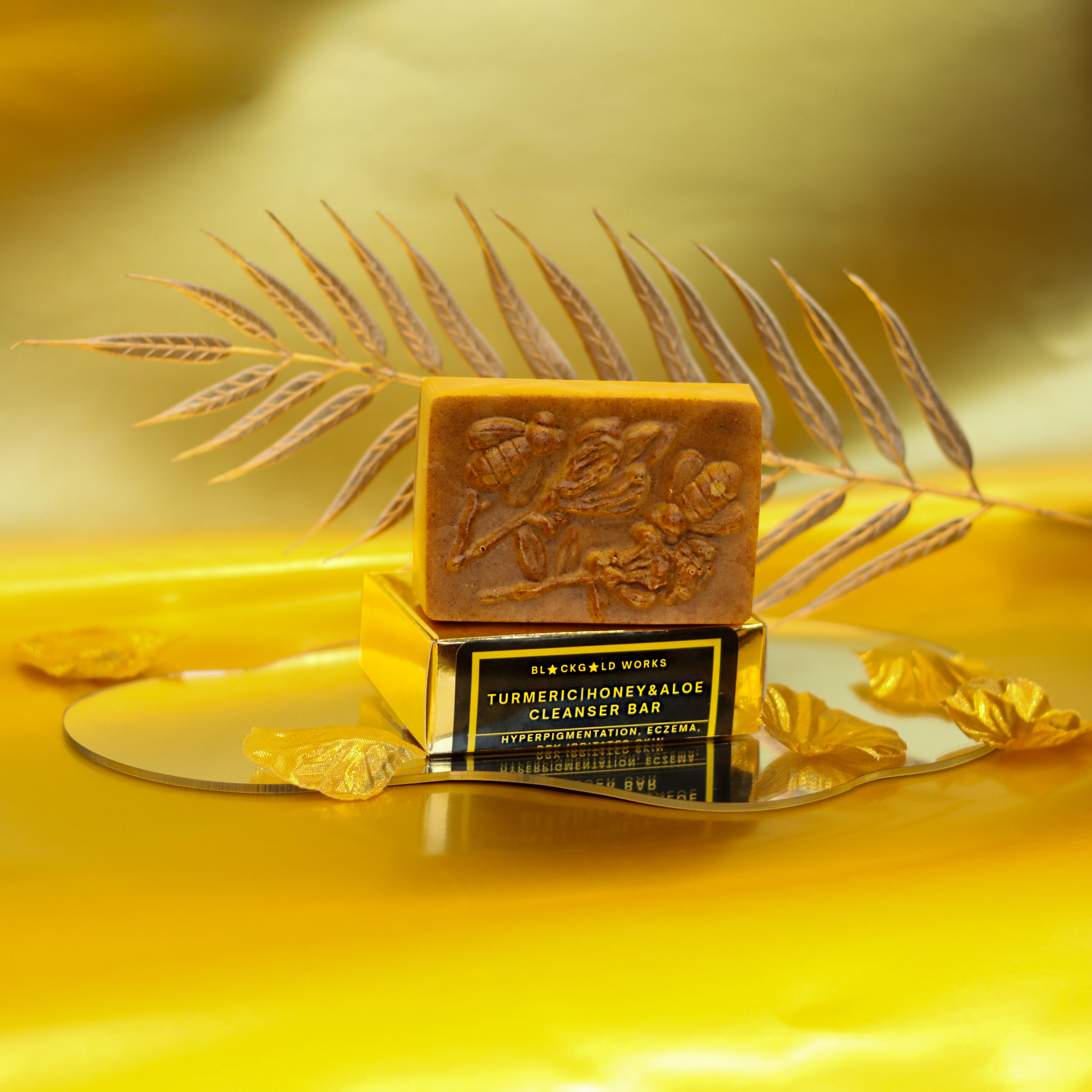 Organic turmeric honey aloe cleanser bar with embossed floral design on top of a gold box with a black and yellow label.