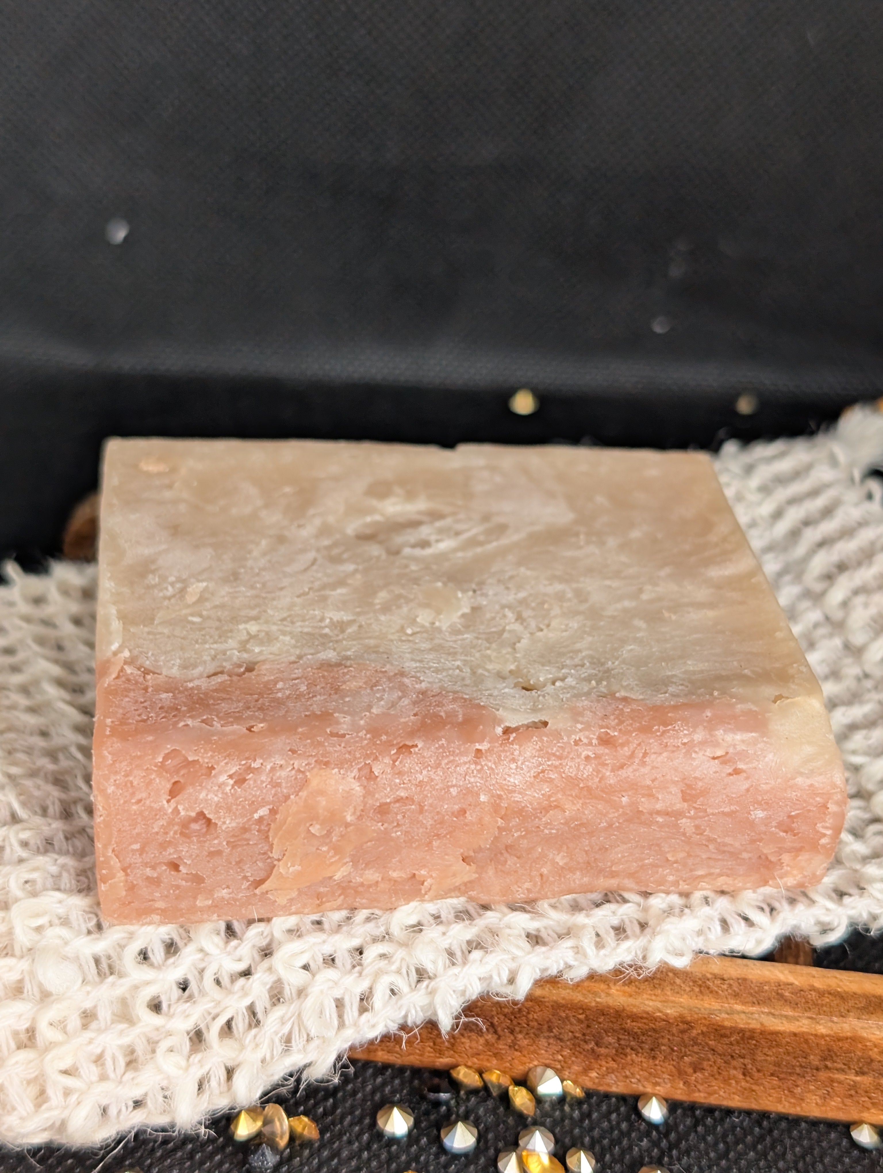 Tan and coral colored rectangular bar of soap on a white mesh rag.